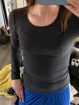 Mörkgrå ribbad långärmad topp - Säljer en mörkgrå långärmad topp med rund halsringning. Toppen är ribbad och har en tight passform som framhäver figuren. Perfekt att styla med jeans eller kjol för en enkel och snygg look.
