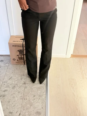 Svarta raka kostymbyxor - Säljer ett par svarta kostymbyxor med rak passform och normal midja. Byxorna har klassisk look och är perfekta till en snygg outfit. Materialet ser ut att vara en mjuk och följsam blandning, troligen polyester eller viskos. Inga synliga detaljer eller loggor. Passar som 34