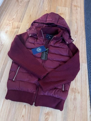 Marcél Classic 02 Hybrid Jacka - Quiltad pufferkropp, stickade ärmar, helzip, avtagbar huva, signaturguldbricka. Lapp kvar, utmärkt skick.