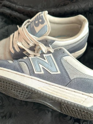 New Balance 480 grå/blå sneakers - Snygga New Balance 480 sneakers i grått och ljusblått med klassisk N-logga på sidan. Skorna har ovandel i mocka och textil, vita snören och perforerad tå för extra ventilation. Tidlös modell som passar till många stilar.