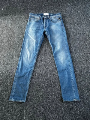 Blå slim fit jeans från Replay - Snygga blå slim fit jeans från Replay med klassisk femficksmodell och diskreta slitningar framtill. Jeansen har normal midja, dragkedjegylf och är tillverkade i mjukt denimtyg som ger en bekväm känsla. Perfekta för en avslappnad och trendig look. Nypris runt ≈ 1500 helt nya!