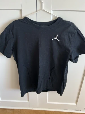 Svart Jordan t-shirt med logga - Snygg svart t-shirt från Jordan med den klassiska Jumpman-loggan broderad på bröstet. T-shirten har rund halsringning och korta ärmar. Tillverkad i mjuk bomull som är skön att bära till vardags.
