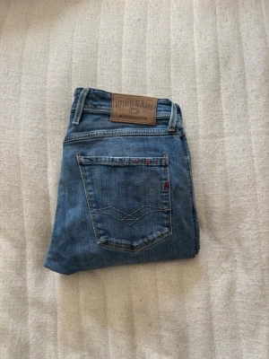 Blå jeans från Replay, modell Anbass - Säljer ett par klassiska blå jeans från Replay, modell Anbass. Jeansen har fem fickor, snygga slitningar och Replay-logga på bakfickan. Tillverkade i mjuk denim med skön stretch och normal passform. Perfekta till vardagslooken!