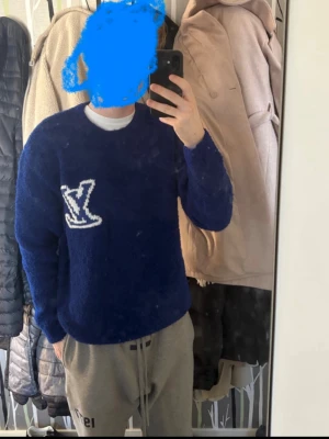 Blå Louis Vuitton tröja - Mörkblå fluffig tröja från Louis Vuitton med stort vitt LV-logotyp på både fram- och baksidan. Tröjan har rund halsringning och långa ärmar. Perfekt för dig som vill ha något både stilrent och lyxigt.