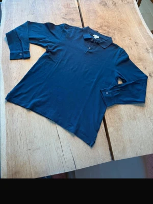 Sunspel pike  - Stilren mörkblå Supima skjorta med klassisk krage och knappar vid ärmsluten. Skjortan har en enkel design och är tillverkad i mjukt bomullstyg som känns skönt mot huden. Perfekt för dig som gillar en clean och tidlös look. Inköpt för 2000 sek och använd kanske 2ggr