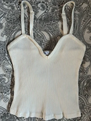 Zara topp - Säljer en vit jättesöt topp från Zara med smala, justerbara axelband och v-ringad urringning. Storlek i S men väldigt liten i modellen! Dock är den stretchig i materialet.