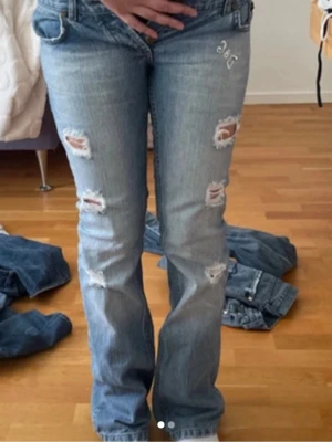 Ljusblå slitna jeans från D&G - Säljer ett par ljusblå jeans från D&G med flera slitningar och hål på framsidan. Jeansen har bootcut-modell och klassisk femficksdesign. Perfekta för dig som gillar en avslappnad och trendig stil. Materialet är denim i bomull.