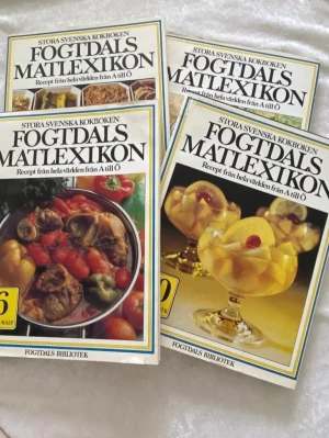 Fogtdals Matlexikon kokböcker - Fyra delar av Fogtdals Matlexikon, en stor svensk kokbok med recept från hela världen från A till Ö. Böckerna har färgstarka omslag med matbilder och tydlig titel i svart text. Perfekt för dig som vill utforska internationella rätter och få inspiration i köket.