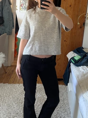 Ljusgrå stickad croppad topp - Säljer en ljusgrå stickad croppad topp med korta ärmar och rund hals. Toppen har en relaxed fit och ribbade kanter vid ärmslut och nederkant. Perfekt att styla med både jeans och kjol för en chill look.