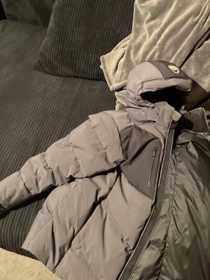 Sail racing antartica jacka - Säljer en grå pufferjacka från sail racing med huva och dragkedja. Jackan har en bröstficka med dragkedja och patch på ärmen. Perfekt för kalla dagar och riktigt snygg streetstil.