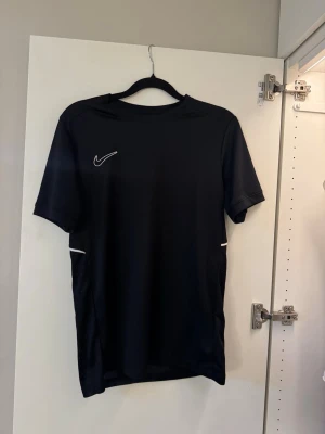 Svart Nike sporttröja - Säljer en svart sporttröja från. Tröjan har korta ärmar och är tillverkad i ett lätt och ventilerande funktionsmaterial, perfekt för träning. (Oklart vilken storlek men känns som S)💙