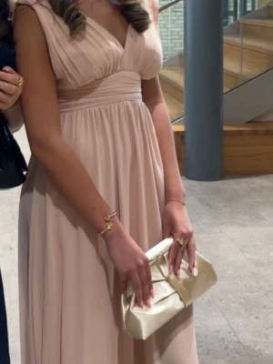 Ljusrosa långklänning med v-ringning - Elegant ljusrosa långklänning med djup v-ringning och veckad överdel. Klänningen har markerad midja och ett flytande, golvlångt kjolparti. Ärmlös design som ger en stilren och feminin look. Perfekt för bal, student eller festligare tillfällen. Andvänd 1 gång, som ny, nypris 1 500 kr! 