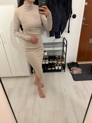 Beige ribbad långklänning Amisu - Säljer en beige ribbad långklänning från Amisu med polokrage och lång ärm. Klänningen har en figurnära passform och är tillverkad i ett mjukt, stretchigt material som sitter snyggt på kroppen. Perfekt för dig som gillar stilrena och enkla looks.