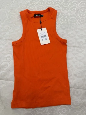 Orange ribbad tubtopp från Bik Bok - Säljer en snygg orange ribbad tubtopp från Bik Bok. Toppen är axelbandslös och har en tight passform som sitter perfekt på kroppen. Perfekt för sommardagar.