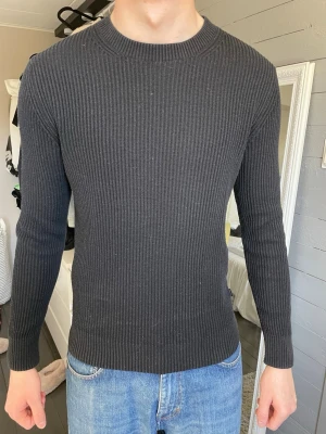 Mörkgrå ribbstickad tröja - Snygg mörkgrå ribbstickad tröja med rund hals och långa ärmar. Tröjan har en smal passform och är tillverkad i ett mjukt, stretchigt material som sitter skönt på kroppen. Perfekt till jeans för en clean look. Säljs pga för liten!