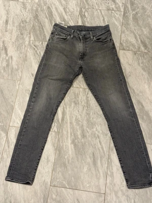 Gråa slim fit jeans från Levi's - Snygga gråa slim fit jeans från Levi's med klassisk femficksdesign och raka ben. Jeansen har en diskret tvättad look och är tillverkade i mjuk denim med stretch för extra komfort. Perfekta för en avslappnad och trendig stil.