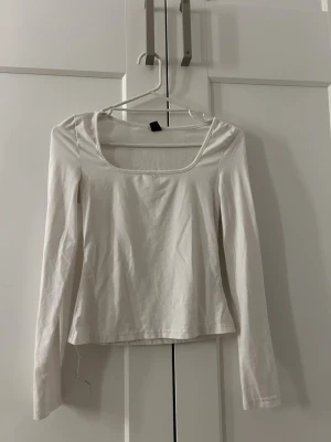 Vit långärmad topp med fyrkantig ringning - En enkel och stilren vit långärmad topp med fyrkantig ringning. Toppen har en normal passform och är tillverkad i mjuk bomull, perfekt att matcha med jeans eller kjol. Inga synliga detaljer eller mönster, bara clean och klassisk vibe.