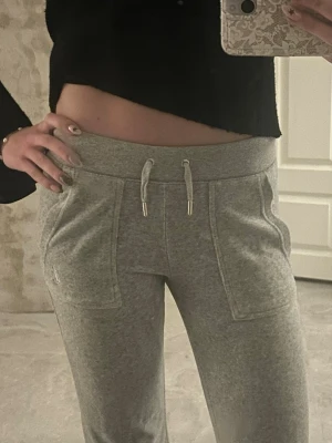 Grå mjukisbyxor Juicy Couture - Säljer ett par grå mjukisbyxor från Juicy Couture med broderad logga på fickan. Byxorna har bred resår i midjan, dragsko och stora fickor framtill. Tillverkade i mjukt och skönt material som passar perfekt för chill dagar.