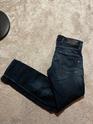 Mörkblå jeans från Replay - Snygga mörkblå jeans från Replay med klassisk femficksdesign och tydliga kontrastsömmar. Jeansen har en rak passform och är tillverkade i slitstark denim med en cool tvätt. Perfekta för dig som vill ha en stilren och tidlös look.