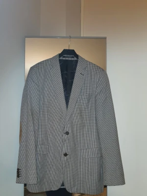 Oscar Jacobson Floyd kavaj, storlek 50 - Kavaj från Oscar Jacobson, 100% ull. Kavajen har två knappar framtill för stängning och fyra knappar vid ärmsluten. Den har två fickor med lock framtill och en bröstficka. Insidan är fodrad med ett mörkt tyg och har flera innerfickor. Se bilder för egen bedömning av skick. Skulle det vara så att man vill göra retur får man gärna det, men man behöver själv stå för returkostnaderna och returen ska ske inom 24 timmar efter uthämtat paket.   #ull #kavajull #ullkavaj