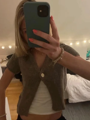 Kort brun stickad kofta - Kort brun stickad kofta med korta ärmar och en stor vit knapp framtill. Koftan har en djup v-ringning och ribbstickade muddar vid ärmslut och nederkant. Perfekt att bära över ett linne för en avslappnad och trendig look. Tröjan är ifrån Zara och är i storleken xs/s🤍 skriv om du har några funderingar eller om du vill ha fler bilder🤍🤍