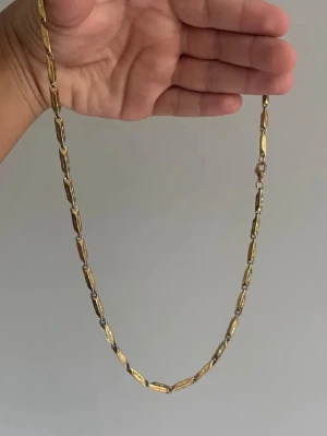 Guldigt kedjehalsband i metall - Snyggt halsband i guldfärgad metall med avlånga, rektangulära länkar. Länkarna har en polerad finish och är sammanlänkade med små ringar. Perfekt för dig som gillar stilrena och trendiga accessoarer.