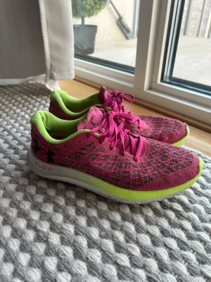 Under Armour rosa sneakers - Snygga sneakers från Under Armour i rosa mesh med svarta detaljer och neongul insida. Skorna har vita sulor med limegröna inslag och rosa snören. Perfekta för dig som gillar sportig stil och vill sticka ut lite extra.