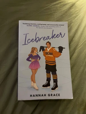 Icebreaker av Hannah Grace - En romantisk och humoristisk roman om konståkaren Anastasia och hockeykaptenen Nate. Omslaget är ljusblått med illustrationer av en tjej i lila klänning och en kille i orange hockeytröja. Perfekt för dig som gillar sport, kärlek och college-vibbar.