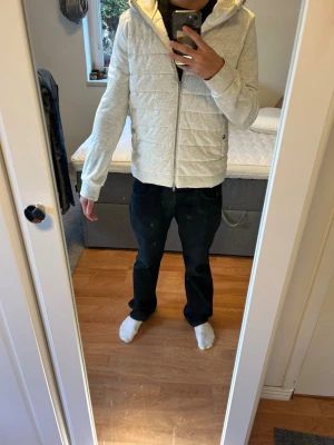 Ljusgrå quiltad hoodiejacka - Snygg ljusgrå hoodiejacka med quiltad framsida och dragkedja hela vägen. Jackan har huva och ribbade muddar vid ärmsluten. Perfekt för lager på lager och chill vardagsstil.