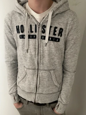 Grå zip hoodie från Hollister - 🌟Storlek S! 🌟Inga defekter!  🌟Priset kan såklart diskuteras✅  Obs! Det står storlek M men passar bättre som storlek S.  Modellen är 180 och väger 65.