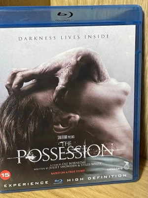 The Possession Blu-ray skräckfilm - Blu-ray-utgåva av skräckfilmen The Possession, regisserad av Ole Bornedal och presenterad av Sam Raimi. Omslaget är grått och blått med en dramatisk bild och text. Filmen är på engelska och rekommenderas från 15 år.