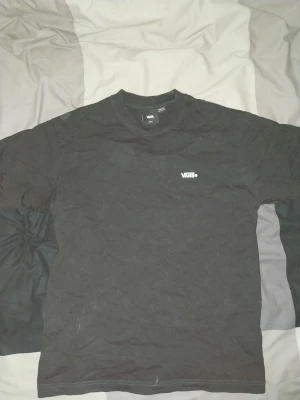 Svart Vans T shirt - Säljer en svart t-shirt från Vans med liten logga på bröstet och stort 'OFF THE WALL' tryck på ryggen. Klassisk passform och rund halsringning. Perfekt för dig som gillar streetwear och enkel stil.