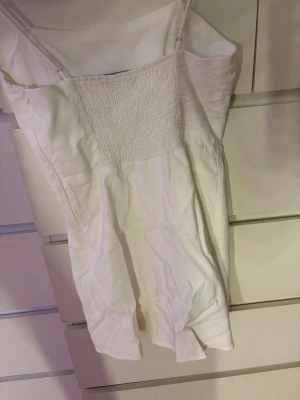 Vit kort sommarklänning med smala band från Zara - Söt vit kortklänning med smala axelband och rynkad detalj över bröstet. Klänningen har en enkel, rak passform. Stilren och enkel design som är lätt att matcha.