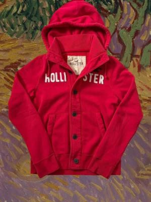 Vintage Hollister button up cardigan - herr strl XL - Säljer en vintage Hollister button up cardigan hoodie i röd färg i storlek XL med vit “Hollister” brodering över bröstkorgen samt vinröd ”Hollister bird”.  👕 Märke: Hollister 📏 Storlek: XL 🎨 Färg: Röd 🧵 Material: 70% bomull, 30% polyester 📐 Mått: 70 cm lång, 57 cm bred 📌 Skick: Mycket bra skick (se bilder)  💬 Hör av dig vid frågor 💰 Pris kan diskuteras vid snabb affär 📦 Skickas inom 24 timmar