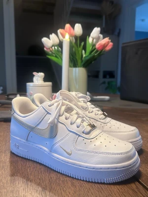 Nike Air Force 1 vita med gulddetaljer - Säljer ett par klassiska Nike Air Force 1 sneakers i vitt läder med guldfärgade detaljer. I storlek 36,5. Använt 1 gång, säljer då de är för små för mig. Köpt för 1200kr, säljer för 800kr. Pris kan diskuteras vid snabb affär.