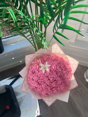 Bukett med rosa rosor och liljor - Säljer en stor bukett med konstgjorda rosa rosor och två vita liljor, inslagen i exklusivt mönstrat papper. Perfekt som dekoration eller present. Blommorna har en mjuk och romantisk look och pappret har ett diskret mönster i ljusrosa.