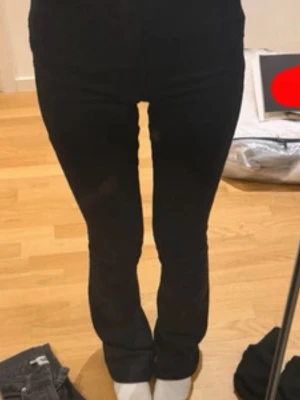 Svarta bootcut jeans med hög midja - Säljer ett par svarta bootcut jeans med hög midja och smal passform över låren. Jeansen har klassisk femficksdesign och stängs med knapp och dragkedja. Perfekta för dig som gillar en tidlös och clean look.
