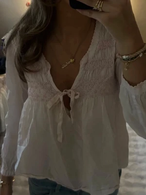 Ljusrosa oss Molly blus med rosett  - Söt vit ljusrosa blus med smock upptill, v-ringning och knytning framtill. Xs/s, från oddmolly. 