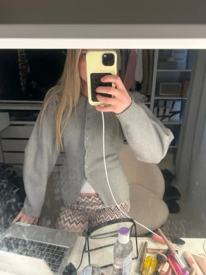 Grå basic kofta med knappar - En enkel och stilren grå kofta med rund hals och knäppning framtill. Koftan har långa ärmar och rak passform, perfekt att slänga över en t-shirt. Materialet ser ut att vara mjukt och bekvämt, troligen bomull eller en bomullsblandning.