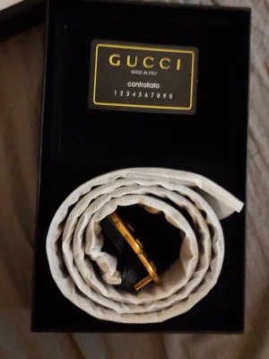Gucci bälte 2298833 FU49X - Äkta Gucci supreme bälte MODEL2298833FU med ikoniskt dubbelt GG-spänne i guld. Bältet har diskret Gucci-logga tryckt längs bandet och är tillverkat i skinn. Perfekt accessoar för att lyfta vilken outfit som helst. Bältet är 105 CM