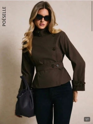 Brun trenchcoat från Shein  - Stilren brun trenchcoat från Poéselle med dubbelknäppning, markerad midja och bälte. Jackan har långa ärmar med knappar vid ärmsluten och en hög krage. Perfekt för dig som gillar klassisk men modern look. Materialet ser ut att vara bomull eller bomullsblandning.