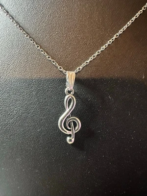 Kedja i rostfritt stål med G-klav hänge - Snyggt halsband i silverfärgad metall med ett hänge format som en G-klav. Kedjan är tunn och stilren, och hänget har en blank finish som fångar ljuset. Perfekt för dig som älskar musik och vill ha en unik detalj till din outfit.