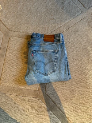 Levi's 501 - Klassiska ljusblå jeans från Levi's med rak passform och fem fickor. Jeansen har en brun läderpatch bak i midjan och den ikoniska röda Levi's-taggen på bakfickan. Tillverkade i slitstark denim, perfekta för en avslappnad och tidlös stil.