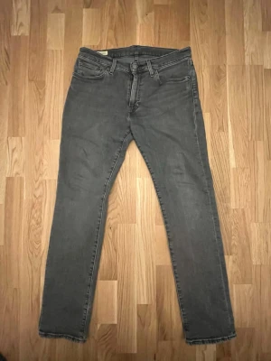 Grå slim från Levis  - Säljer ett par grå slim fit jeans med klassisk femficksdesign och dragkedjegylf. Jeansen har raka ben och är tillverkade i ett mjukt denimtyg som ger en skön passform. Perfekta för dig som gillar en enkel och stilren look.