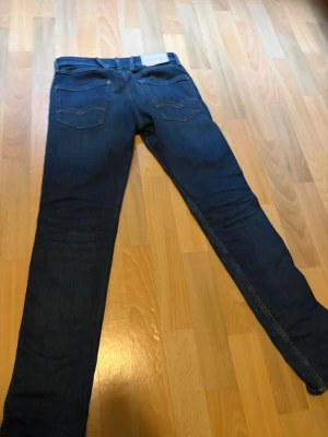 Mörkblå slim fit jeans från replay anbass - Säljer ett par mörkblå slim fit jeans med klassisk femficksdesign och kontrastsömmar. Strl 28W 30L