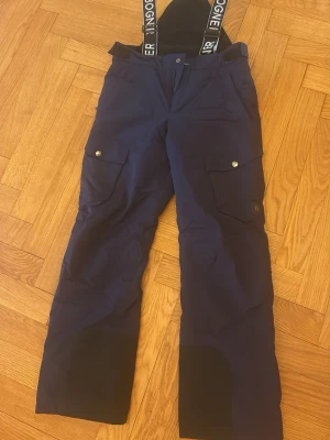 Mörkblå skidbyxor från Bogner - Säljer ett par mörkblå skidbyxor från Bogner. Byxorna har stora fickor med lock och tryckknappar samt ett B-märke på ena benet. Skick: 9.5/10😮‍💨⛷️. Storlek finns på bild. Perfekta för vintersport och outdoor.