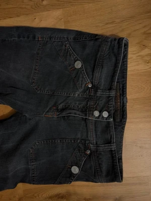 Mörk gråa bootcut lågmidjade jeans med detaljer - Säljer ett par mörkgråa bootcut & lågmidjade jeans med mycket detaljer och unika utan fickor. Jeansen är utsvänga och kontrastsömmar i orange på framsidan. De är helt felfria! Skriv privat för mer information🥰