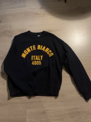 Svart sweatshirt Monte Bianco - Cool svart sweatshirt med gul text 'MONTE BIANCO ITALY 4805' på bröstet. Klassisk rund halsringning och långa ärmar. Perfekt för dig som gillar streetwear och vill ha en enkel men snygg tröja med tryck. Helt ny, har bara dragit av lappen.  ❤️