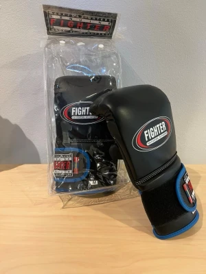 Svarta boxningshandskar Fighter M - Säljer ett par svarta boxningshandskar från Fighter med blå detaljer och kardborrestängning. Hanskarna är 8oz. Handskarna har vit söm och logga på ovansidan. Perfekta för träning inom boxning eller kampsport. KÖP 2 FÖR 400