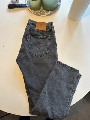 Grå Levi's straight jeans - Snygga grå jeans från Levi's med klassisk rak    passform. Jeansen har en läderpatch bak i midjan och den ikoniska röda Levi's-taggen på bakfickan. Tillverkade i slitstark denim, perfekta till vardagslooken. Storlek W32L34